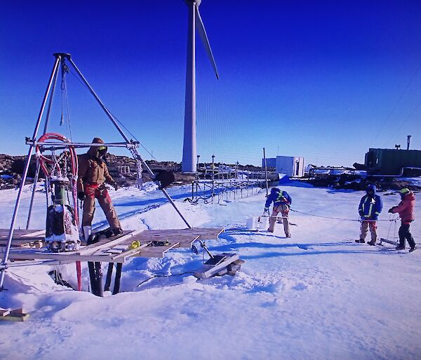 Expeditioners working on the melt bell with a large tripod to support the equipment.