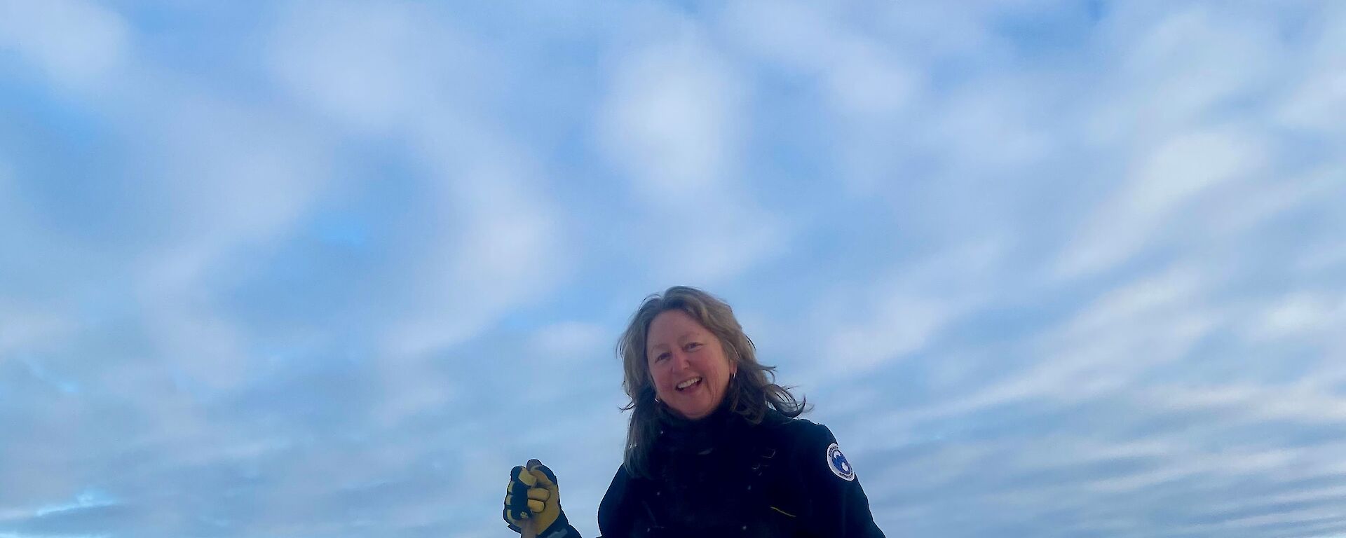 A woman stands next to a hole in the sea ice smiling to camera