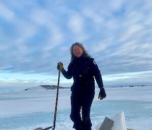 A woman stands next to a hole in the sea ice smiling to camera