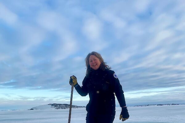A woman stands next to a hole in the sea ice smiling to camera
