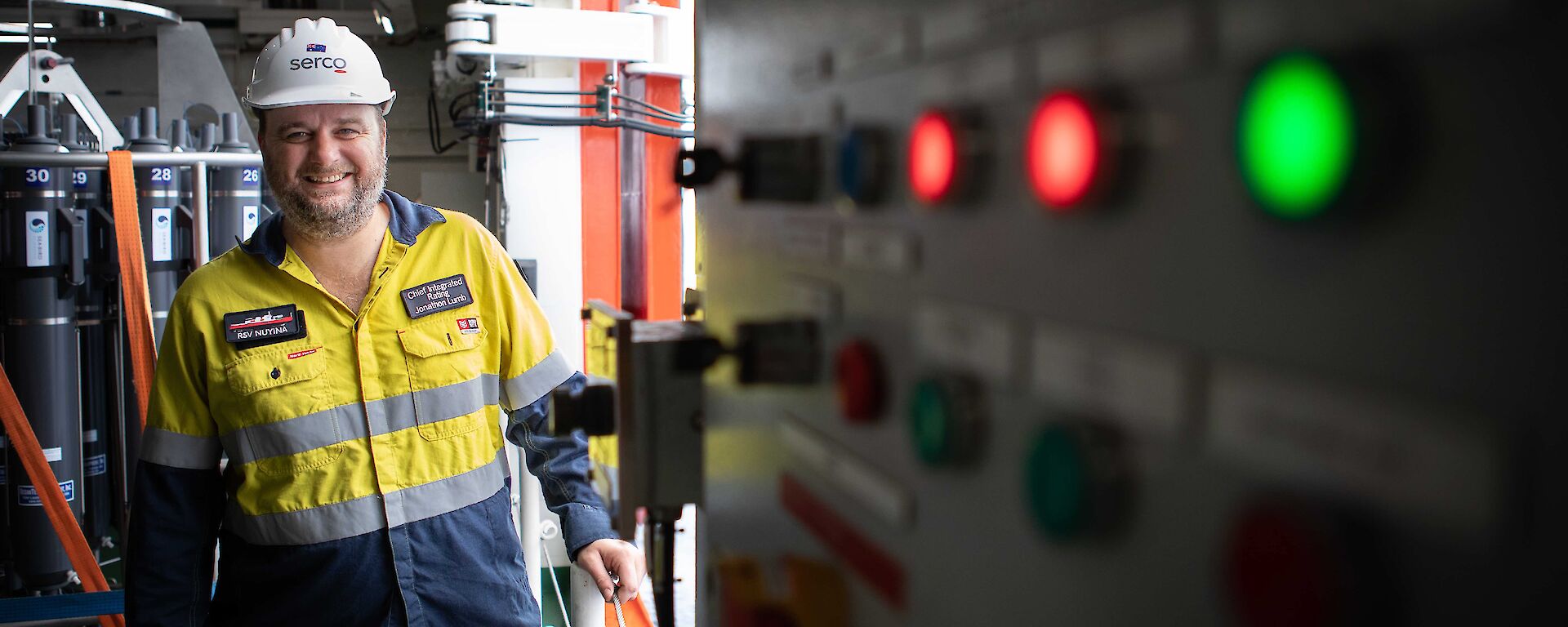 Man in hi vis standing next to a lit up switchboard