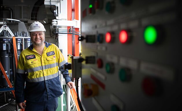 Man in hi vis standing next to a lit up switchboard