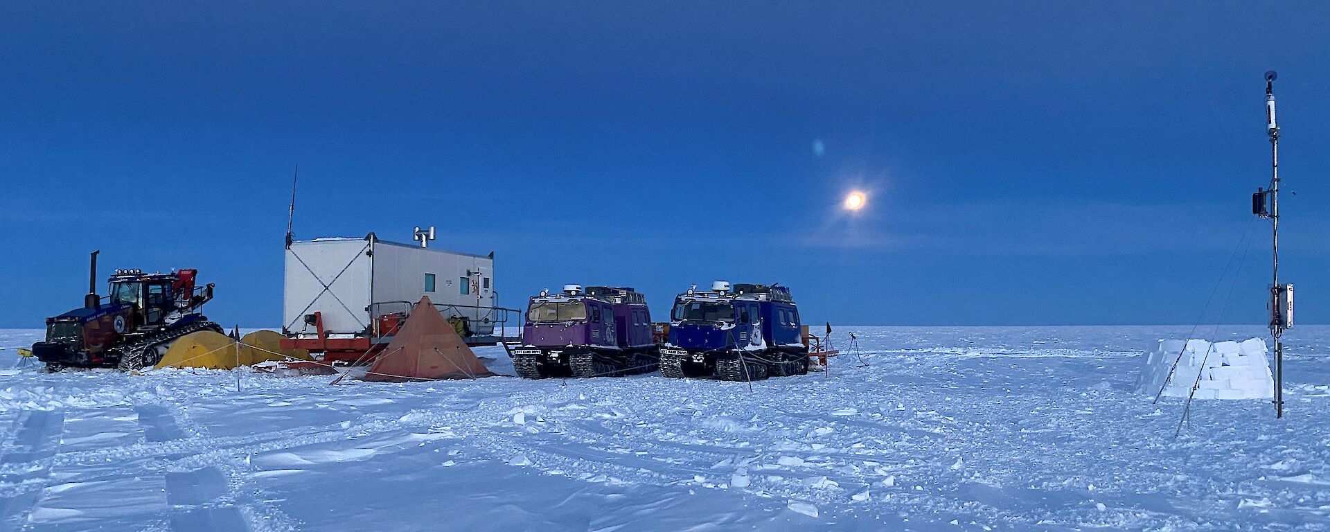 An icy campsite of tents and vehicles is lit by the moon