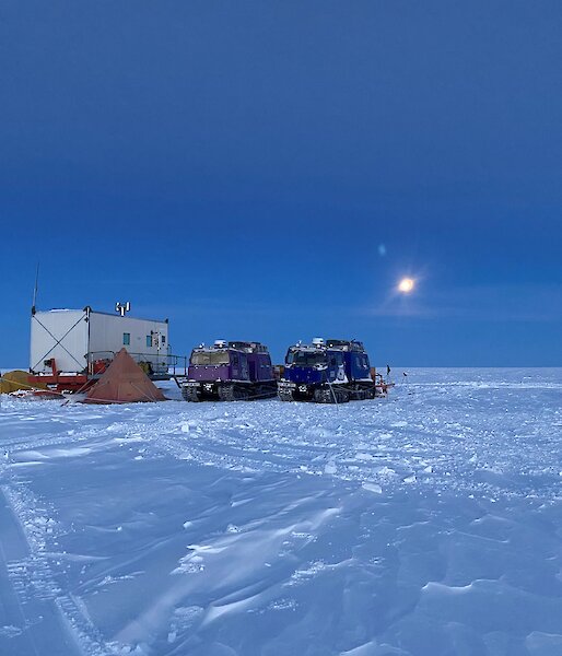 An icy campsite of tents and vehicles is lit by the moon