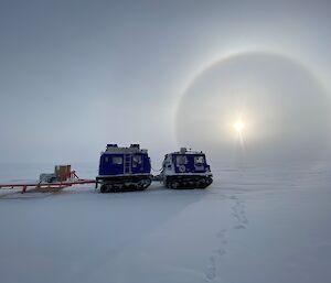 A large blue vehicle sits on the snow lit by the sun