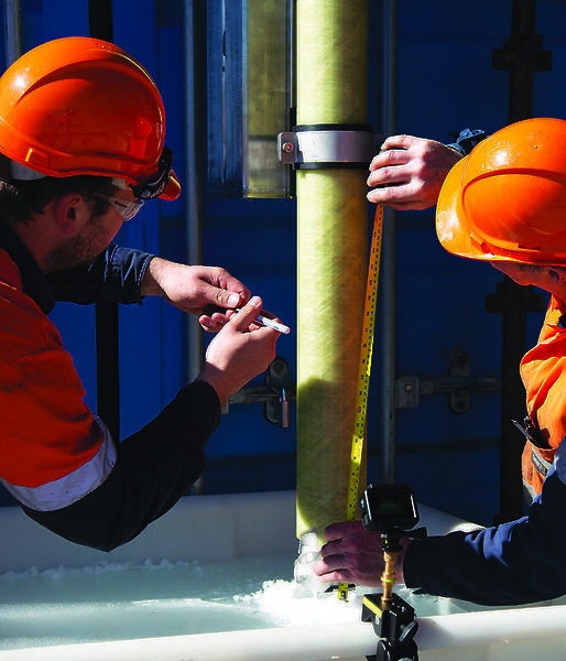 Two men in hi-vis and hard hats measuring the length of a drill pipe suspended over a block of ice