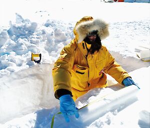 A man in cold weather gear standing in a snow trench measuring an ice core