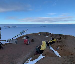 Three person team repairing an Automatic Weather Station on a rocky outcrop