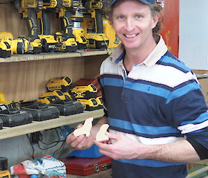 Man standing in front of shelves of wood-working tools, holding two wooden penguins
