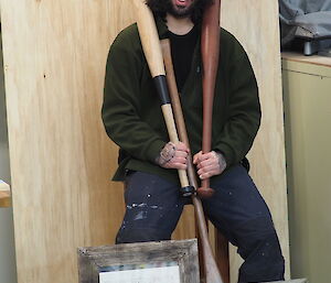 A man shows off his hand made bats, an oar and two picture frames
