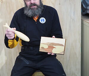 A man displays his hand made timber whale and a marquetry picture