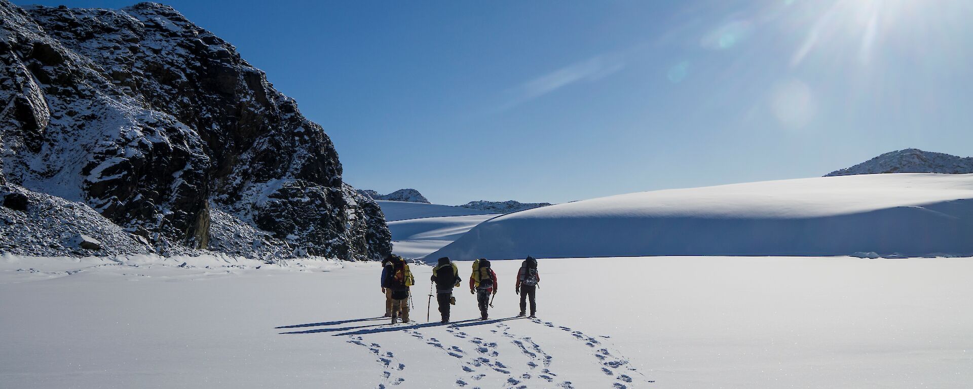 4 people walk through untouched snow in the sunshine