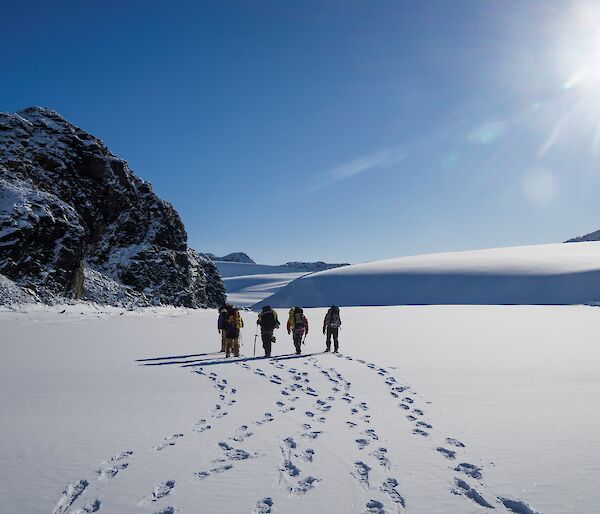 4 people walk through untouched snow in the sunshine