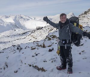 A man poses for the camera in front of a dramatic backdrop of snowy hills