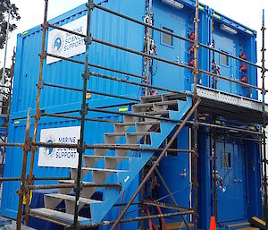Two blue shipping containers stacked on top of another two blue shipping containers.