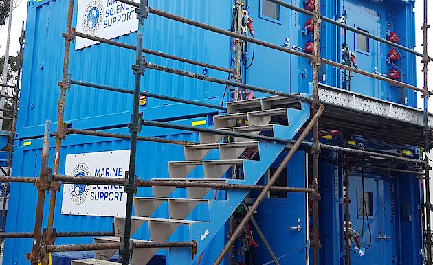 Two blue shipping containers stacked on top of another two blue shipping containers.