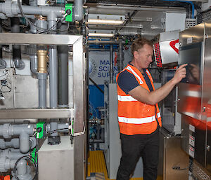 Man standing at a control panel in a mechanical plant room.