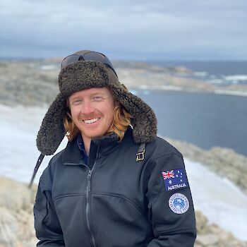Expeditioner Pat Burchett wearing Antarctic cold weather clothing, with bay in the background