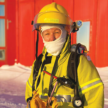 Expeditioner Robyne Chawner wearing yellow fire fighting clothing and helmet, and carrying equipment.