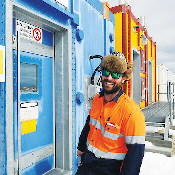 Electrician Wayne Donaldson poses outdoors by door of station building.