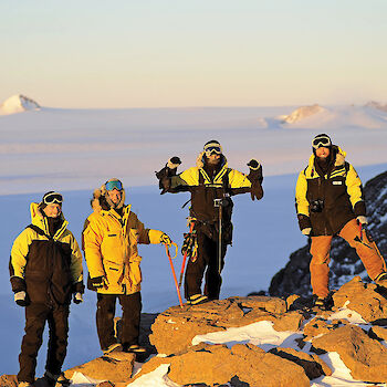 Four expeditioners stand on a rocky mountain surface with the ice plateau behind.