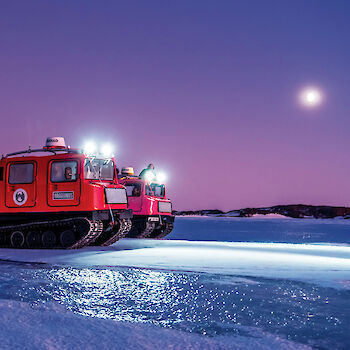 Moon in a pink and purple sky shining about oversnow vehicles.