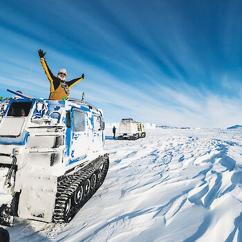Expeditioner with arms outstretched in the roof of the oversnow vehicle parked on the ice.