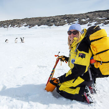 Expeditioner kneeled in snow watching penguins.