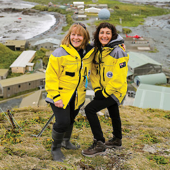 Two female station leaders on a hill overlooking Macquarie Island station buildings.