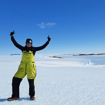 Expeditioner raising hands in joy in icy landscape.