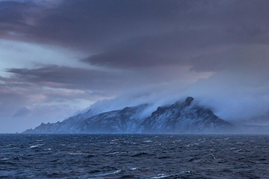A dramatic landscape with choppy sea before an island emerges covered in low lying cloud