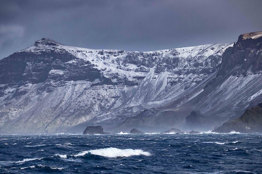 A dramatic sea scape with white snow dusted cliffs in the background