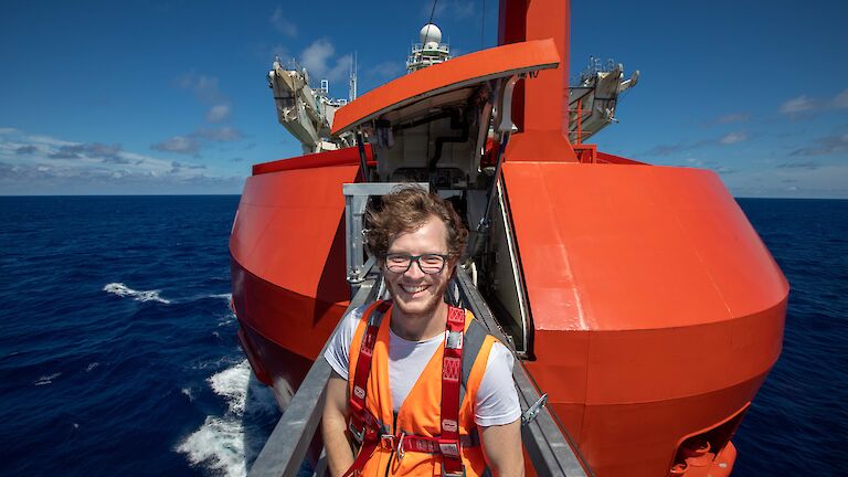 A man standing on a metal walkway sticking out of bow of the ship over the water