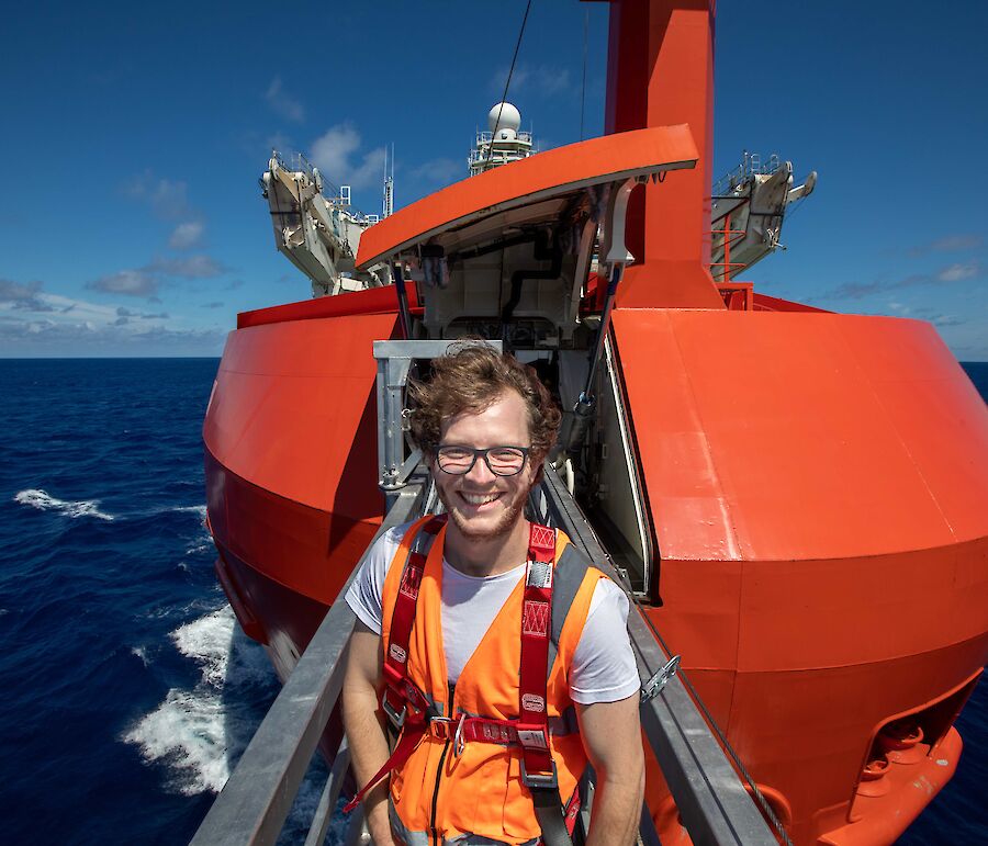 A man standing on a metal walkway sticking out of bow of the ship over the water