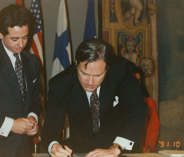 A man signing a paper, with another looking on.