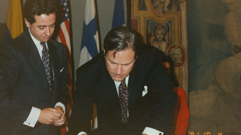 A man signing a paper, with another looking on.