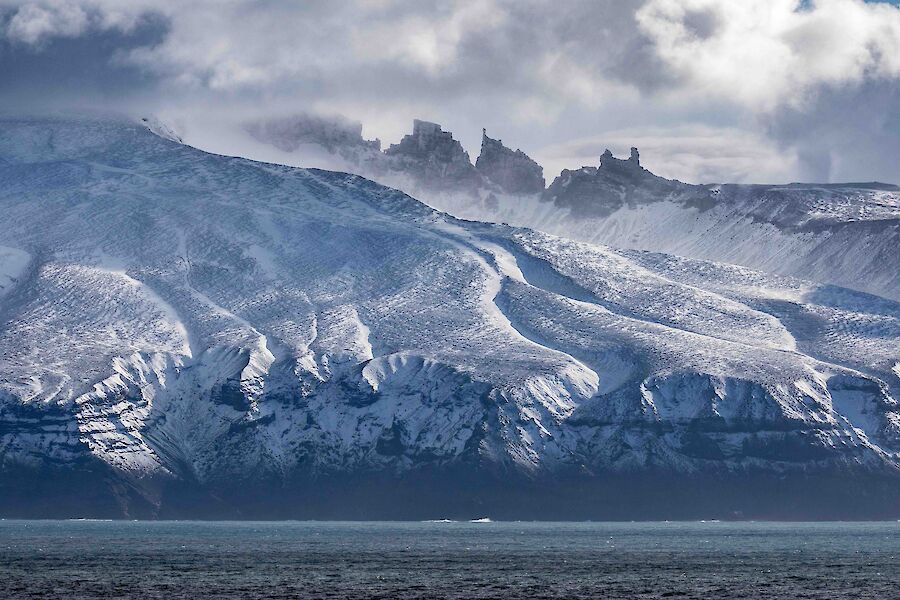 Dramatic, snow dusted cliffs and mountains rise up from the sea.