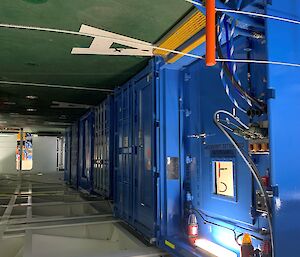 blue shipping containers inside a ship's hold. Services provided to container through pipes and cables