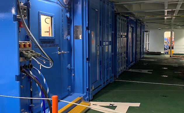blue shipping containers inside a ship's hold. Services provided to container through pipes and cables