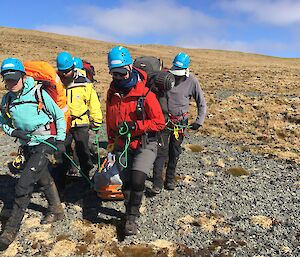 Four people carry a stretcher over rocky terrain