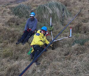 Two people on the side of a hill arranging ropes to allow a stretcher to be lowered down