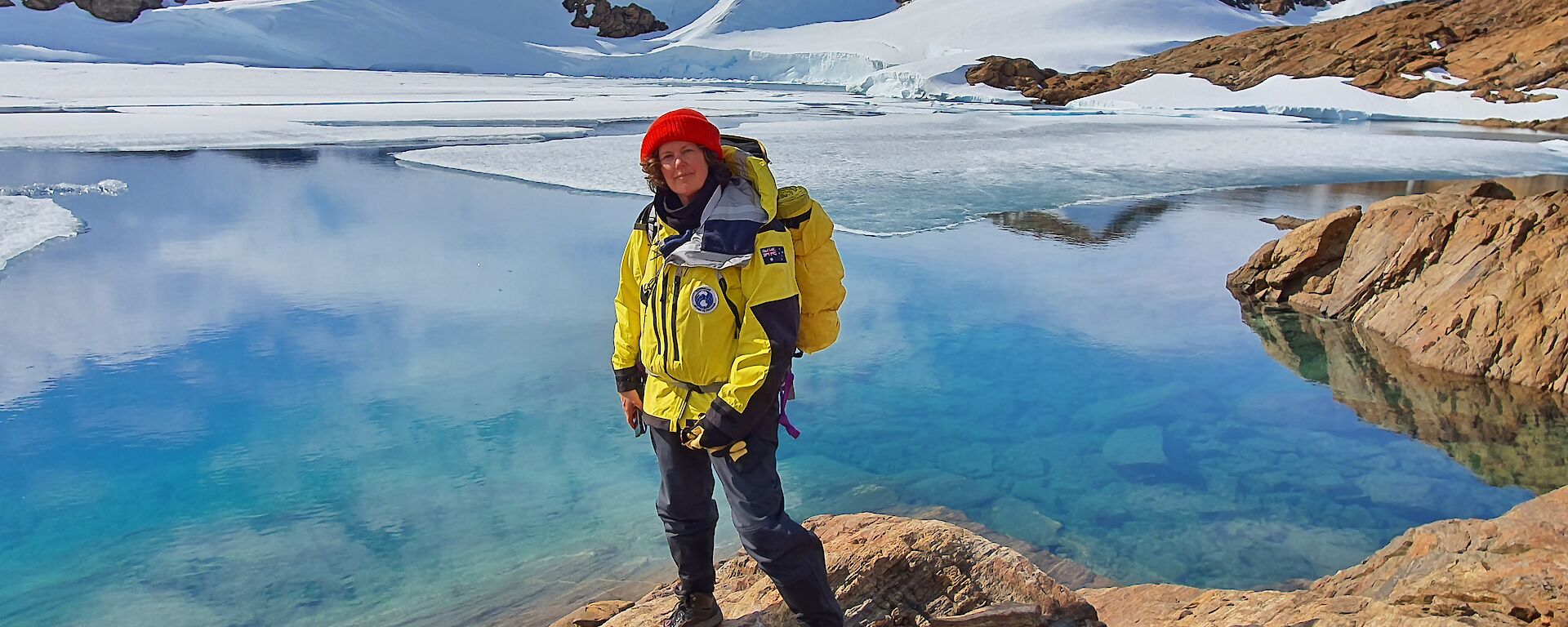A woman in cold weather gear standing in front of a beautiful blue icy lake