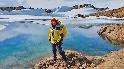 A woman in cold weather gear standing in front of a beautiful blue icy lake