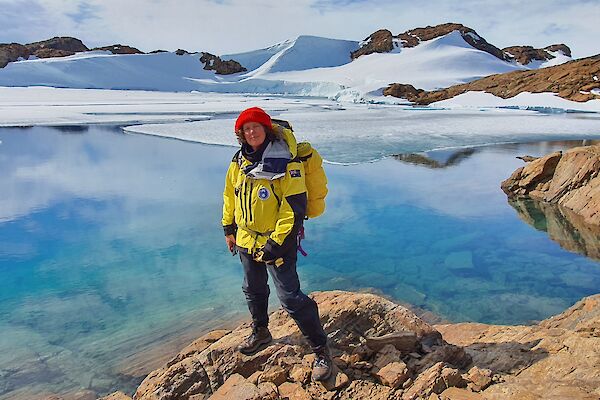 A woman in cold weather gear standing in front of a beautiful blue icy lake