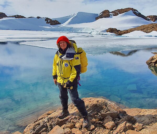 A woman in cold weather gear standing in front of a beautiful blue icy lake