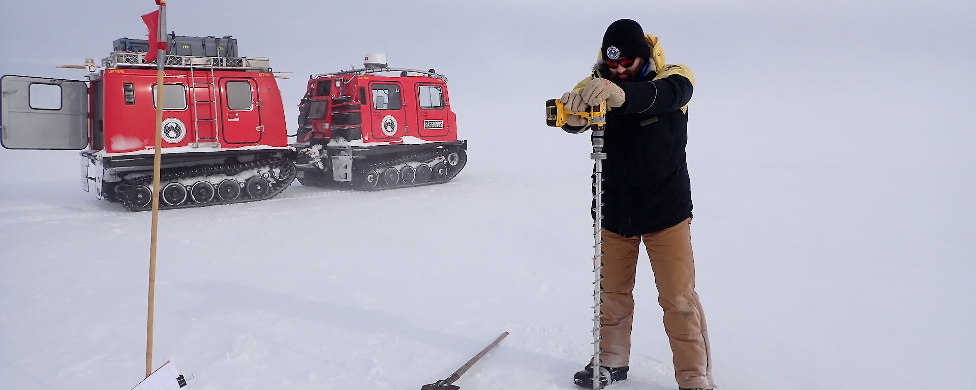 A man drills the sea ice in front of a red vehicle