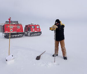 A man drills the sea ice in front of a red vehicle