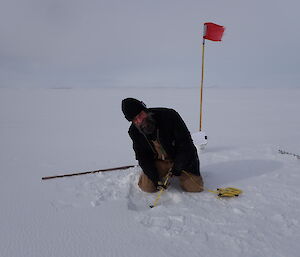A man measures the thickness of the sea ice with a tape measure down the hole