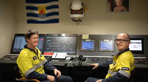 Two men sit at the controls in the engine room