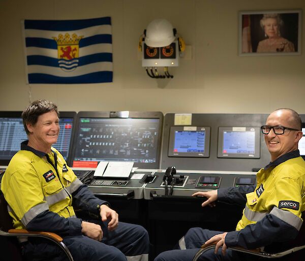 Two men sit at the controls in the engine room